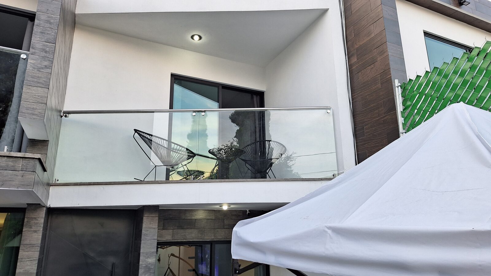 Balcón con barandal de vidrio y sillas acapulco